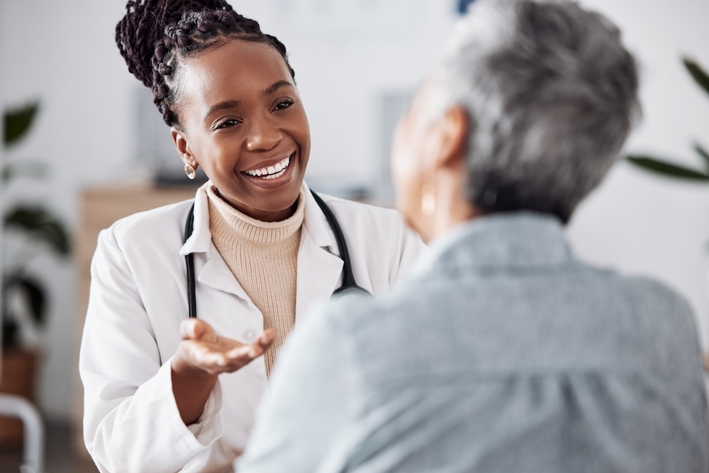 Smile, black woman or doctor consulting a patient in meeting in hospital for healthcare feedback or support. Happy, medical or nurse with a mature person talking or speaking of test results or advice